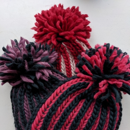 Three hats in different colours with large pompoms