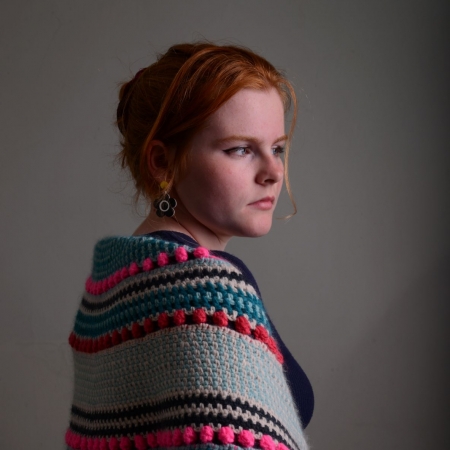 Woman wearing crochet shawl around her shoulders looking right into the distance